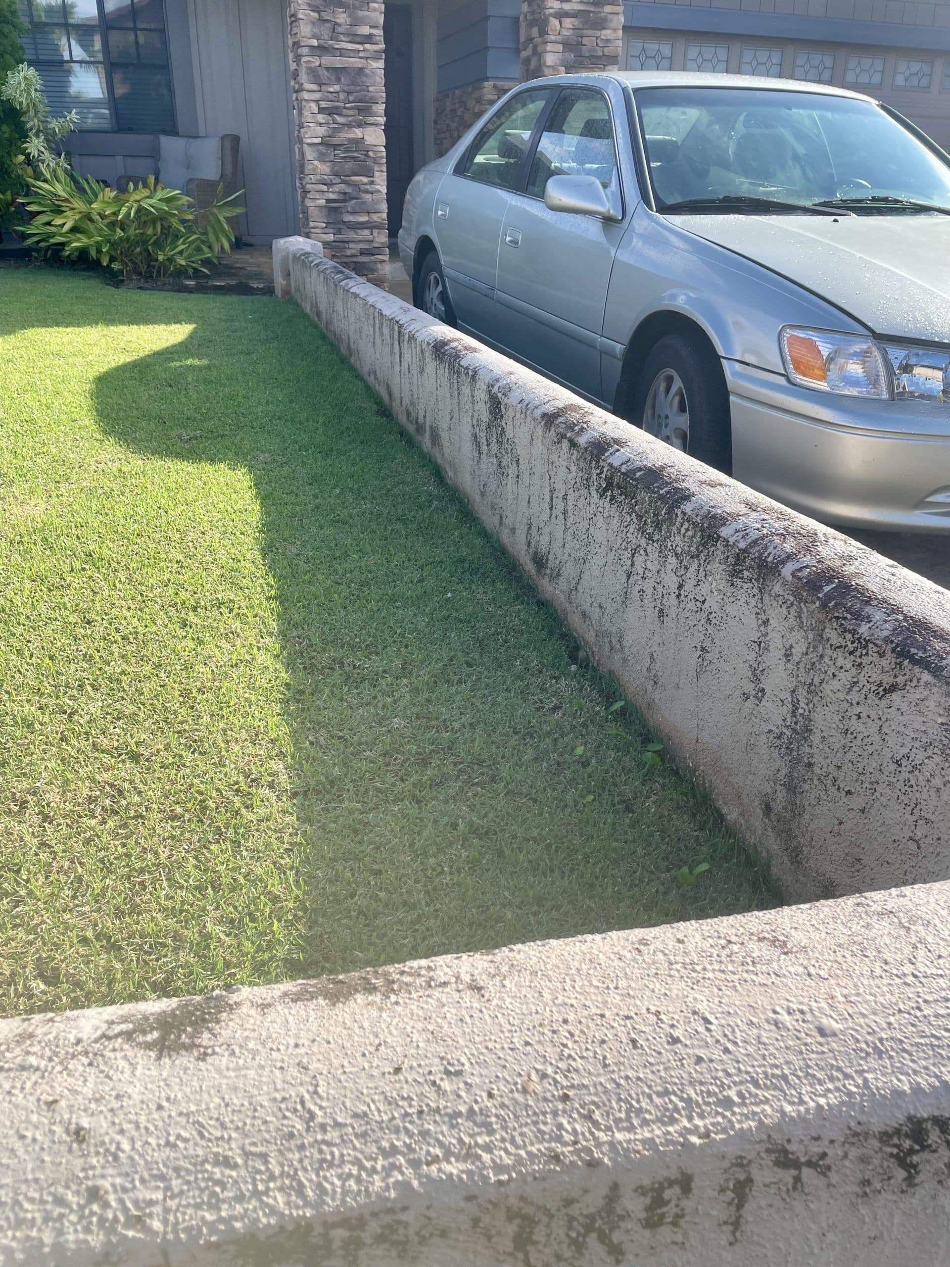 Silver car parked beside a concrete barrier in a well-maintained grassy yard.