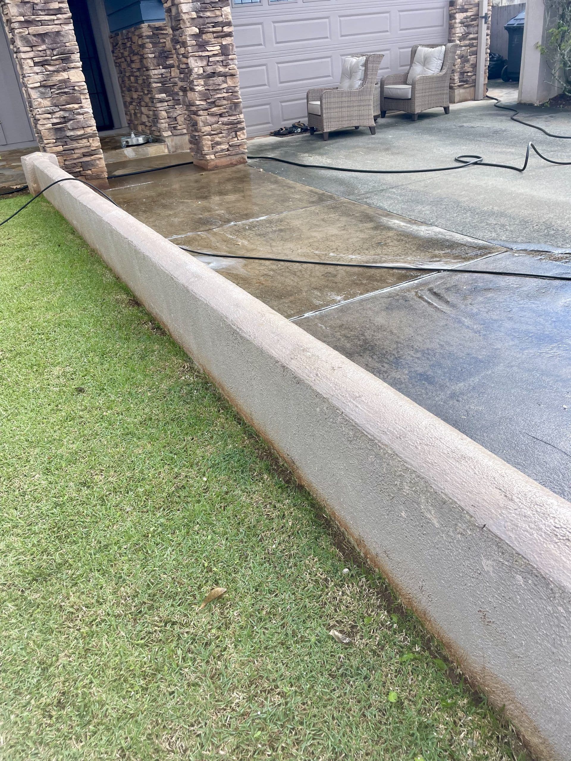 Clean concrete border along a driveway with green grass and patio furniture in the background.